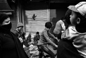 A monochrome photograph of an people walking on the streets of old delhi, a shadow of a bird on the back